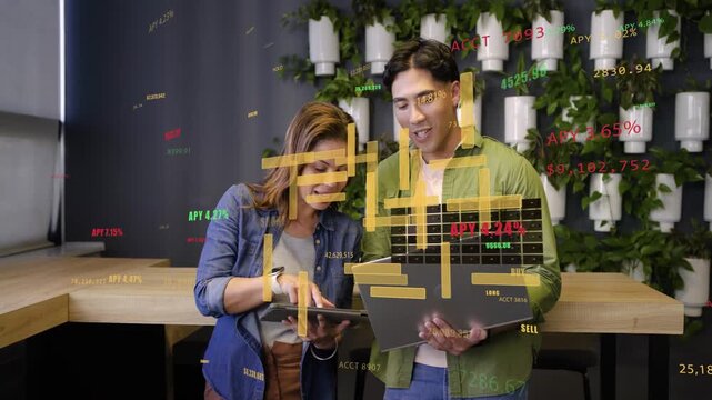Leaning coworkers examining tablet while tilting laptop at wooden counter showing data charts