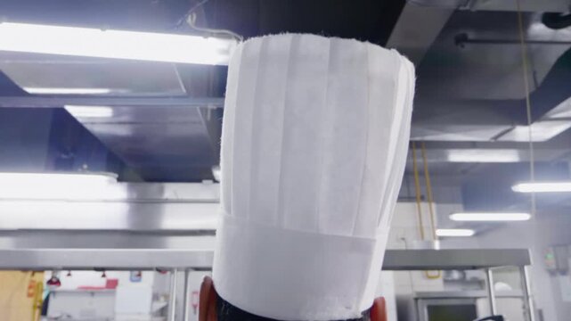 Slow Push-In Behind Unrecognizable Chef Putting On Tall White Hat in Commercial Kitchen - 60fps