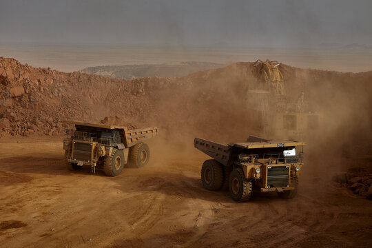 An ultra-class mining haul truck powers across the vast floor of an open-pit mine, kicking up a trail of fine dust as it moves with surprising purpose and precision for a machine of its extraordinary 