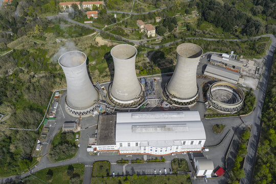 Larderello, Italy - 10 April 2026: Aerial view of the Enel Green Power geothermal power plant with three large cooling towers and industrial buildings nestled in the green hills of Tuscany.