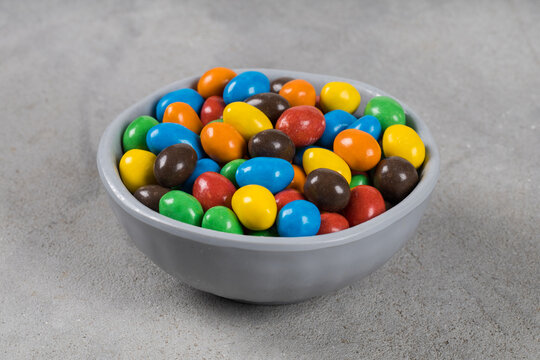 Vegan MultiColored Dragees with peanuts and chocolate. In a bowl. Light gray background. Close-up	
