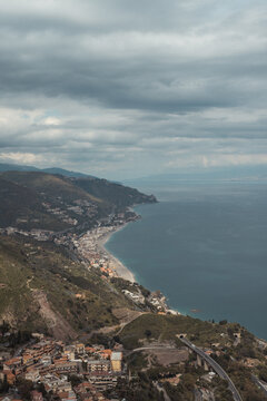 View of the stunning coastline where the town meets the sea under a cloudy sky, a serene blend of architecture and nature, Taormina, Sicily, Italy.