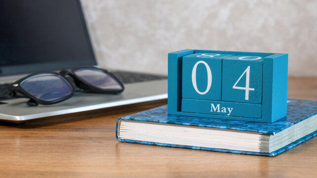 Wooden block calendar showing May 04 on a desk with a laptop and eyeglasses, representing planning and business concepts