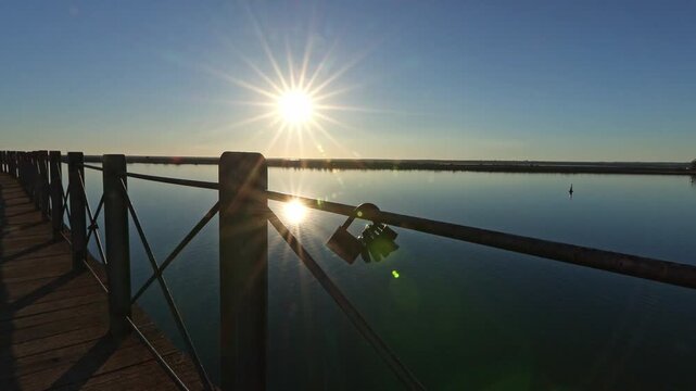 Close up of love locks on the railing of the historic iron pier. Golden sunstar reflecting on the calm Odiel river at dusk. Huelva, Andalusia, Spain