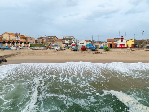 Aerial view of vibrant beach huts nestled along the sandy shore contrasting with the turbulent ocean waves, Vila Cha, Porto, Portugal.
