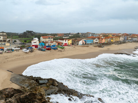 Aerial view of vibrant, colorful houses stand boldly against the serene, sandy beach, where fishing boats rest and waves crash, Vila Cha, Porto, Portugal.