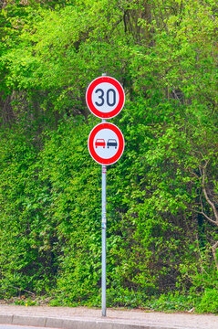 Roadside speed limit and no overtaking signs against a lush green foliage background