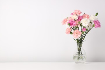 Obraz premium Beautiful carnation flowers in vase on white table, space for text