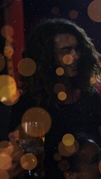 Vertical video: Central person laughing clinking beer as offscreen friend raising glass in bar glow