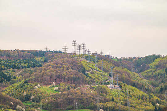 Towering power lines traverse lush green hills and dense forests under a cloudy sky
