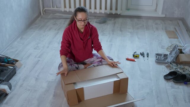 Lady Arranges Items After Unpacking. Asian Woman Tidies Space After Carefully Unwrapping Parcels. An Asian Woman Efficiently Organizes Her Space After Opening Packages And Removing Contents