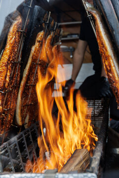Closeup Of Handmade Smoked Mackerel. Market Vendor Tends Traditional Smoked Fish Over Glowing Embers