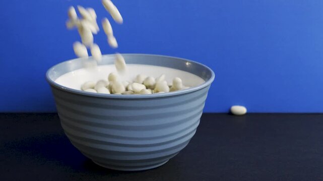 White_beans_pouring_into_bowl_on_blue_background_10bit_120fps