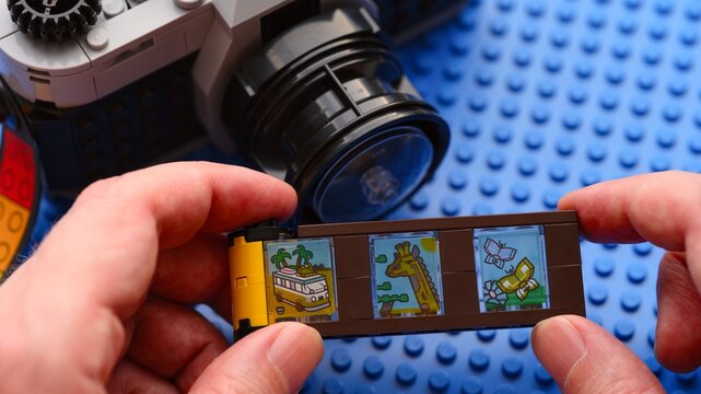 Tambov, Russian Federation - February 20, 2026 Person hands holding a toy film strip from the Lego Creator 3in1 Retro Camera building set with a vintage-style brick-built camera on the background.