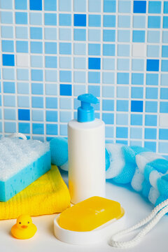 Natural baby soap bar in dish and cosmetic bottle with blue bath accessories and sponge.