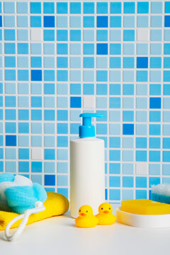 Baby bath products set with shampoo pump bottle, two small rubber ducks and yellow sponge on blue tile background.
