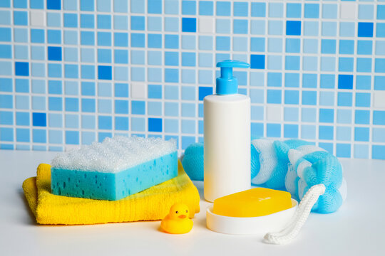 Baby bathing essentials and skincare products on white table against blue mosaic wall.