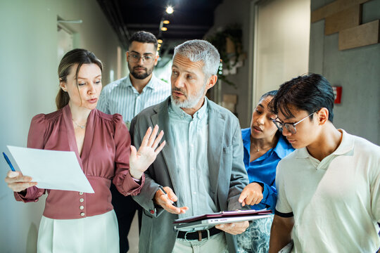 Coworkers reviewing project plan in modern office hallway