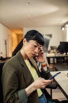 Pensive businesswoman checking smartphone in modern office