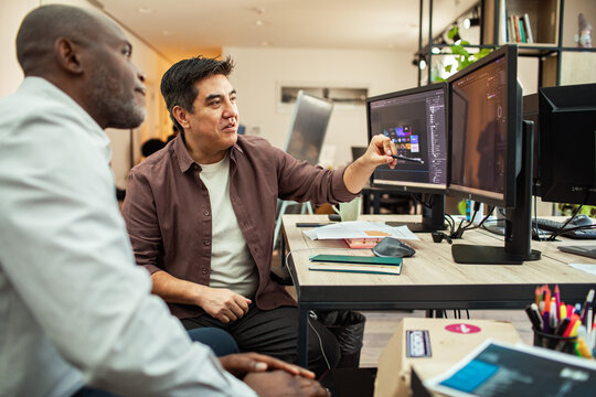 Coworkers collaborating on design at dual monitors in modern office