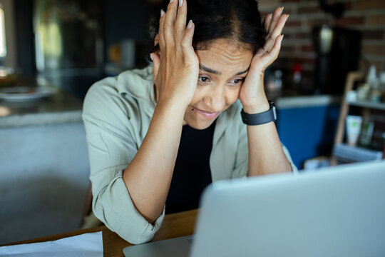 Frustrated woman working on laptop in home kitchen