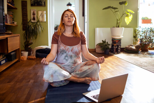 Woman meditating with laptop in cozy home living room