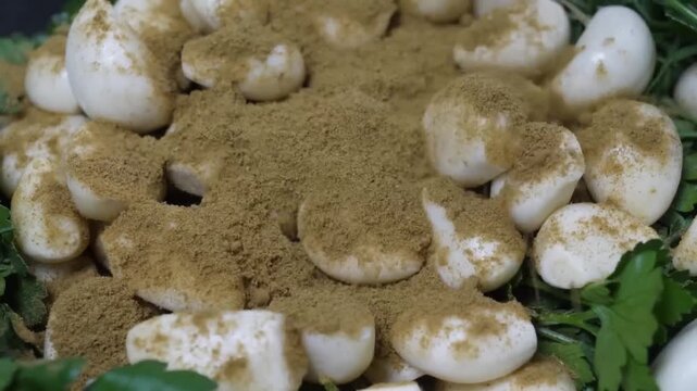 A high-resolution, close-up shot of fresh, peeled white garlic cloves. Some cloves are plain, while others are lightly dusted with a brown spice, possibly cumin or coriander.