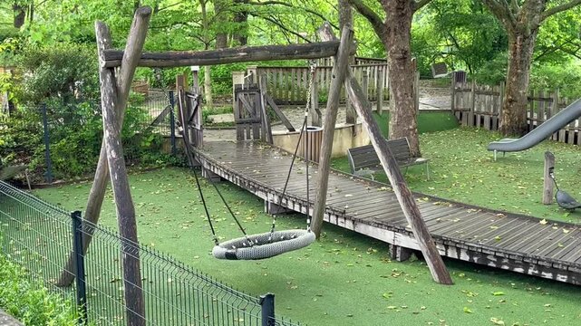 Slightly moving empty swing in the park playground for kids, rest and relax natural background template, no children, loneliness sadness concept, ground is wet after rain
