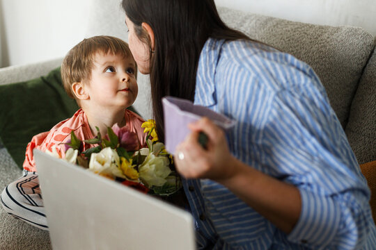 Cute child boy giving bouquet to beautiful mother on mothers day.  Happy Mother's day! Stylish Mom and son spending time together on couch at home, family holidays