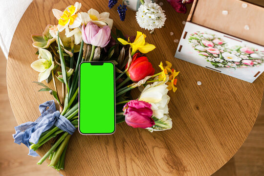 Empty phone screen, beautiful bouquet and gift box on wooden table, view above. Happy Mother's day! Digital Greeting card mock up with space for text. International women's day. Phone template