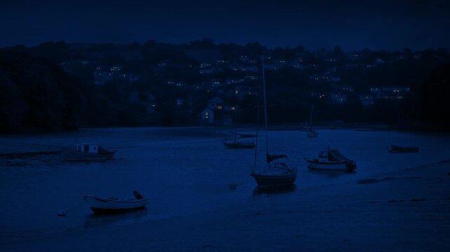 Boats In Bay At Night With Houses Lit Up In The Distance
