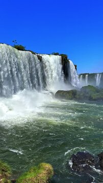 Breathtaking panoramic view of Iguazu Falls in Brazil, powerful waterfalls cascading into the river with lush green vegetation and clear blue sky, travel footage