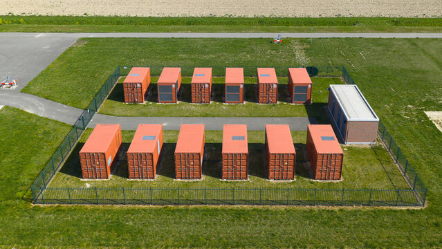 Aerial view of orange battery storage containers arranged in rows within a fenced industrial area surrounded by green fields Middelharnis, Zuid-Holland, Netherlands.