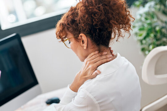 Tired mature woman with neck pain looking uncomfortable while working on a computer in the office