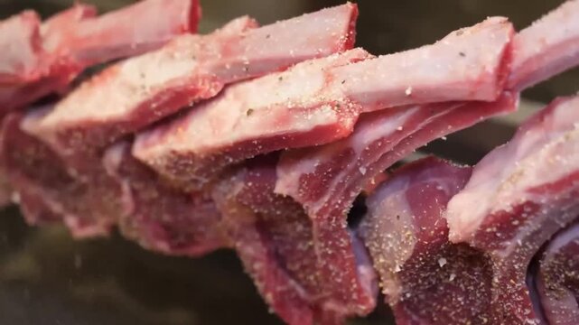 Close-up footage of fresh, raw beef ribs or chops, lightly seasoned with salt and pepper, displayed in a butcher shop or meat market counter. This footage is ideal for food-related projects, cooking s