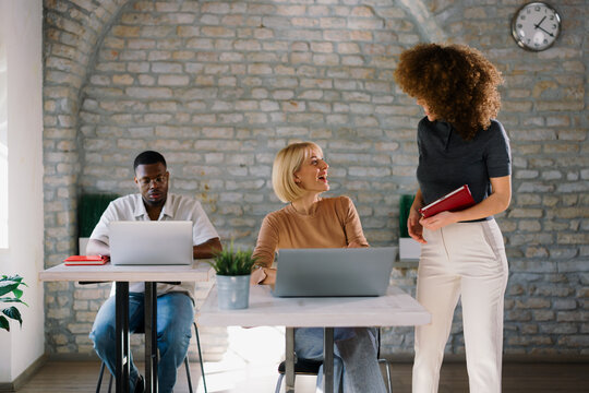 Coworkers discussing project in office while working on laptops