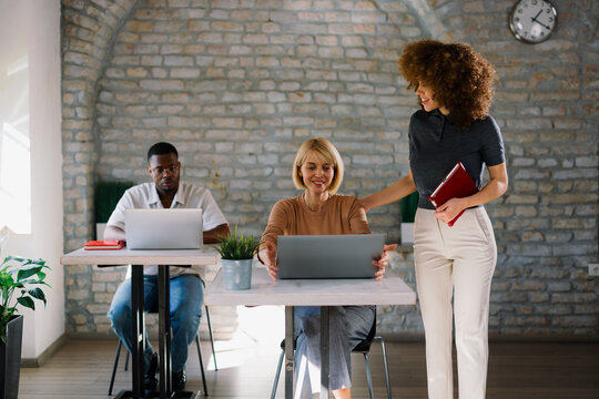 Diverse coworkers collaborating on tasks using laptops in bright contemporary workspace