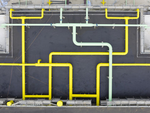 Aerial view of industrial yellow and light green pipes arranged in a geometric pattern on a dark rooftop in Taiwan.