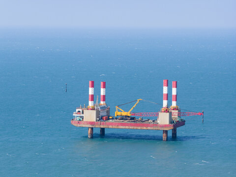 Aerial view of an offshore construction platform with red and white striped towers and a yellow crane in the blue sea Taiwan.