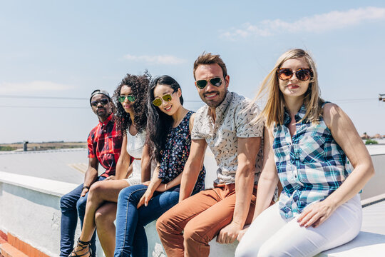 Diverse friends in sunglasses relaxing on a rooftop ledge
