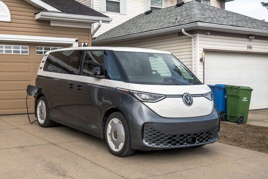 Calgary, Alberta, Canada. April 15, 2026. A grey and white Volkswagen ID. Buzz electric van charging in a residential driveway.