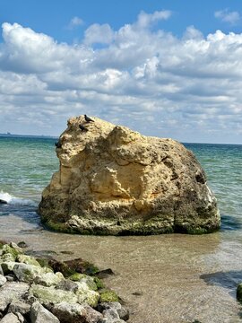 A scenic landscape featuring a massive yellow sandstone boulder standing in crystal clear sea water. Several pigeons rest on top of the rock