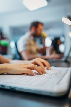 Closeup of hands typing on laptop in busy office