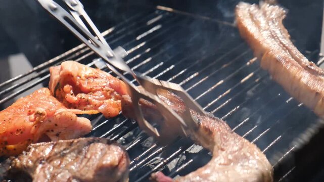 Grill chef uses cooking tweezers to turn barbecue pieces of fried fatty meat with appetizing look on hot grate producing smoke and aroma. Pork ribs fried in spices on open fire.