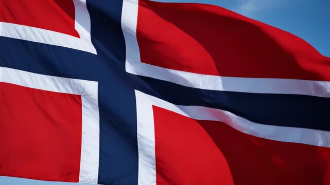 Close-up of a Norwegian flag waving in the wind against a clear blue sky, showcasing the red field with a blue Nordic cross outlined in white and visible fabric folds and motion