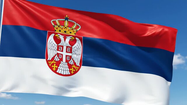 Waving Serbian national flag with prominent coat of arms featuring double-headed eagle and crown, tricolor horizontal bands of red blue and white fluttering against bright blue sky