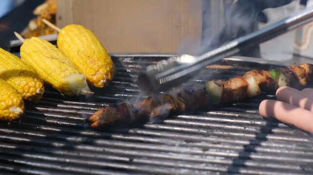 Barbecue chef cuts hot kebab on skewers with knife checking meat doneness. Juicy grilled meat roasted on open fire at outdoor gastronomic festival with smoke and aroma.