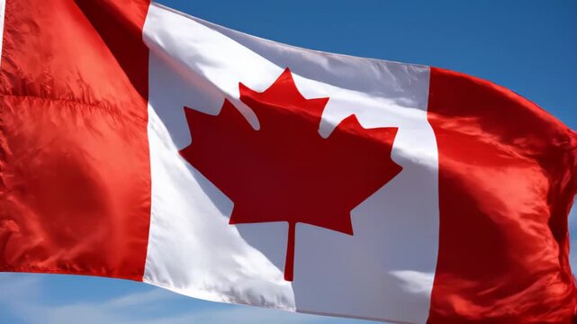 Large Canadian national flag with red maple leaf waving against a clear blue sky, closeup of fabric folds and motion capturing patriotic symbolism and outdoor celebration