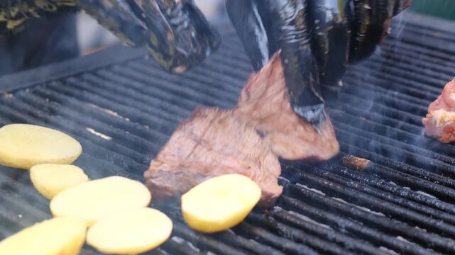Chef hands in black gloves turn and remove beef steak from grill, checking doneness for safe eating. Juicy fried beef on open grill grate in outdoor meat restaurant. Outdoor meat cuisine.