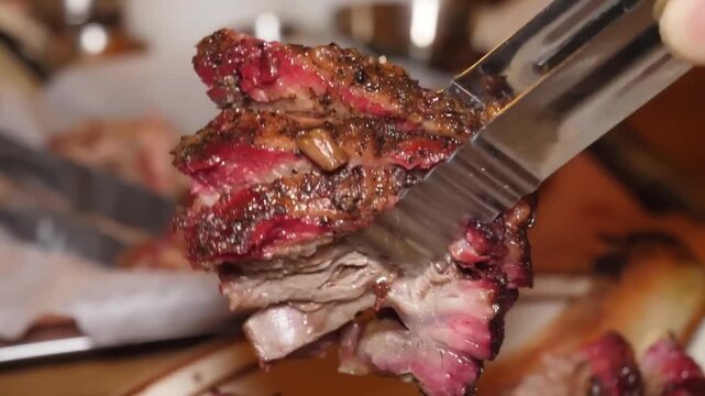close-up shot of a hand using metal tongs to pick up a slice of perfectly cooked, juicy smoked brisket from a serving plate. The meat has a prominent pink smoke ring and is glistening with natural jui